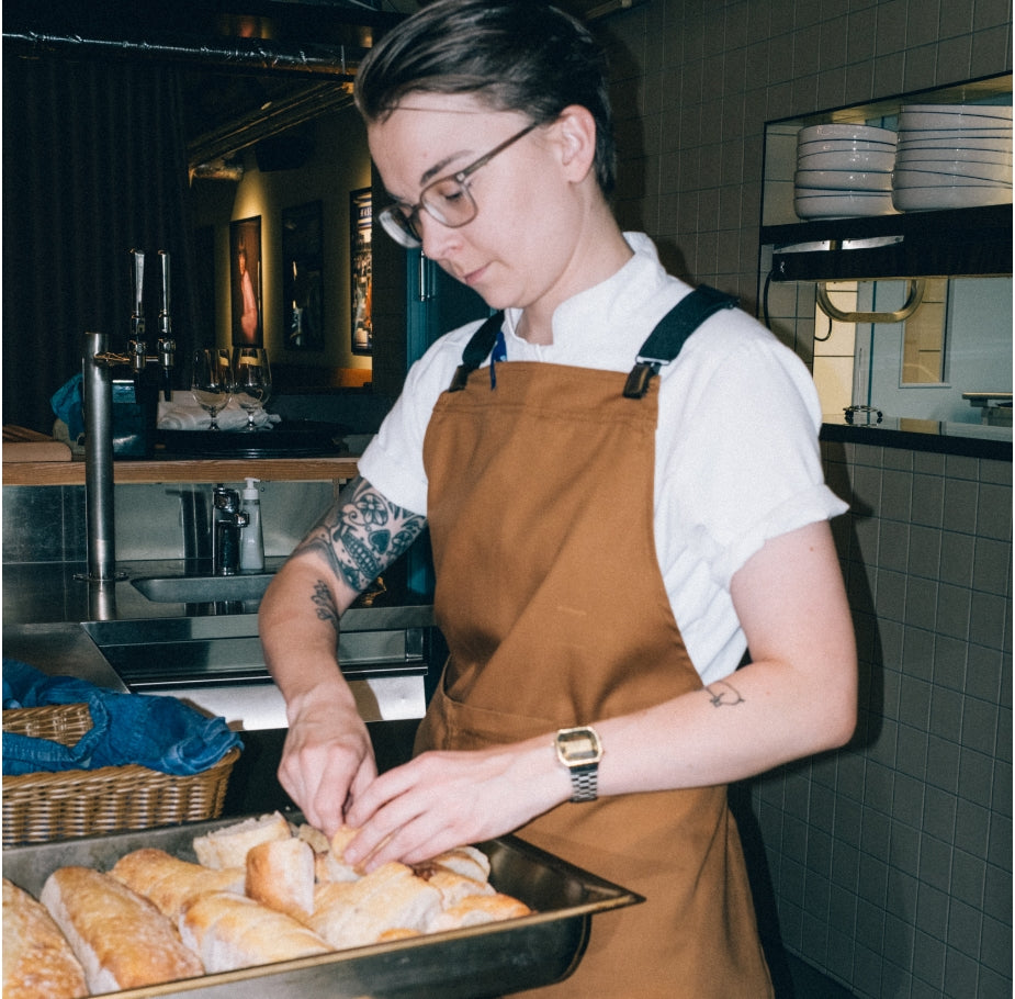 Kock i brunt förkläde och vit kockrock skär bröd i en restaurangkök.